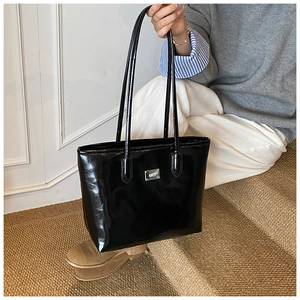 Chic black patent leather tote bag with silver metal plaque in an urban lifestyle setting