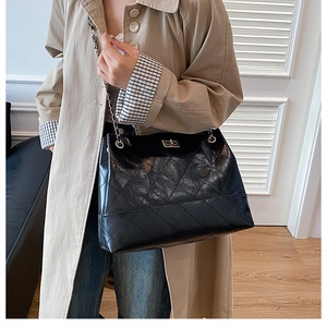Vista laterale di una borsa tote in pelle trapuntata nera con catena su un trench beige