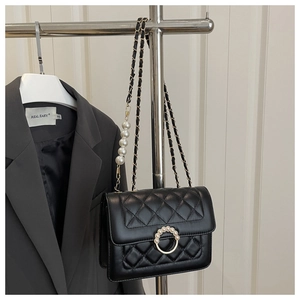 Detail of black quilted leather bag featuring gold hardware and pearl chain strap
