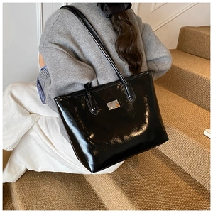 Lifestyle view of a glossy black patent leather bucket bag with silver metal plaque