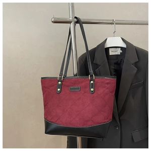 Detail of burgundy quilted tote bag with black faux leather trim and fashion patch