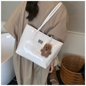 Detail of a creamy white glossy tote bag with a cute brown plush bear charm accessory