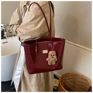 Detail of dark red glossy leather tote bag on model's shoulder with plush bear charm