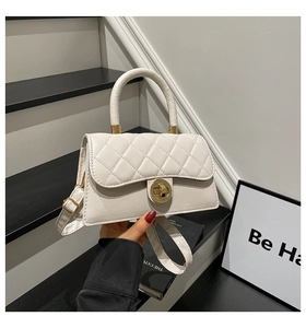 Detalle de bolso acolchado blanco con cierre de giro dorado y asa en un entorno minimalista