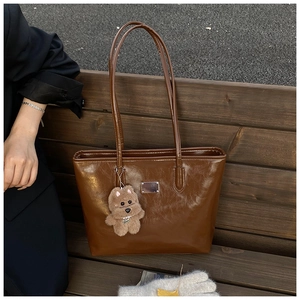 Detailed texture of brown glossy leather tote bag with a cute plush dog charm on side