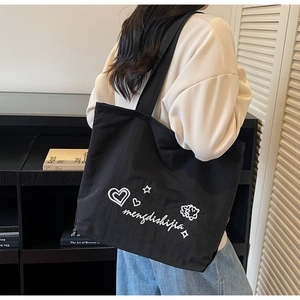 Détail d'un cabas en toile noire avec broderie blanche et large bandoulière souple