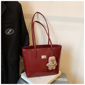 Detail of glossy red bucket tote bag with metal hardware and cute teddy bear pendant