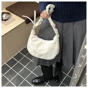 Detail of white pleated moon bag featuring a scrunched handle and elegant fashion text