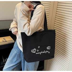 Détail d'un sac cabas en nylon noir avec motifs de cœurs blancs porté à l'épaule du mannequin