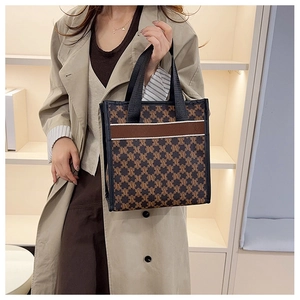 Detail of printed tote bag with M-pattern and brown strap on a beige coat background