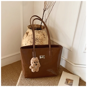 Brown leather tote bag with elegant metal hardware and a cute plush bear accessory