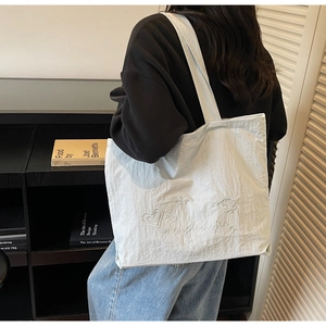 Vue détaillée du sac cabas blanc en nylon avec broderies d'étoiles et de cœurs sur l'anse