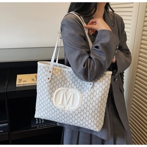 Close-up of white tote bag with gray M-letter print and oval embossed logo detail