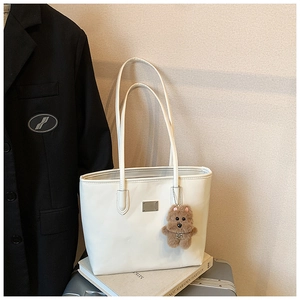 Detail of white PU leather tote bag with gold metal plate and brown plush bear charm