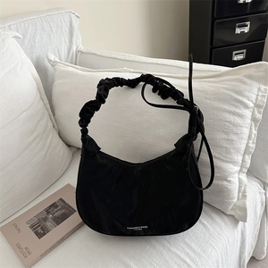 Black crescent shoulder bag with scrunchie strap and satin finish on a white sofa