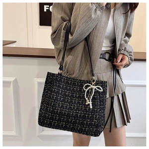 Details der Tweed-Eimertasche mit schwarz-goldener Textur und Perlen-Schleifen-Anhänger