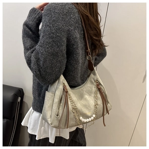 Detail of silver shoulder bag with pearl accents and brown strap shown on a model