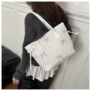 Detail showing white tote bag with colorful embroidered bows and textured finish