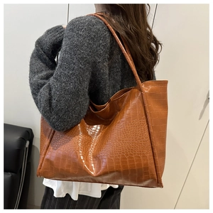 Side view of large brown crocodile embossed tote bag worn by model for size reference