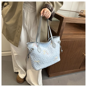 Detail of light blue quilted tote bag with embroidered letters and beaded bows