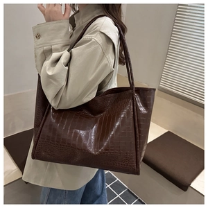 Detail of dark brown tote bag with crocodile texture and long shoulder straps