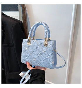 Close-up of light blue crossbody bag with quilted embroidery and woven handle detail