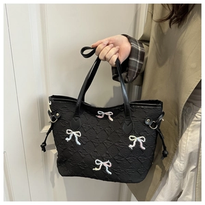 Detail of black quilted tote bag featuring colorful beaded bows and leather handles