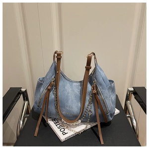 Detailed view of light blue denim tote bag with brown leather straps and pearl chain