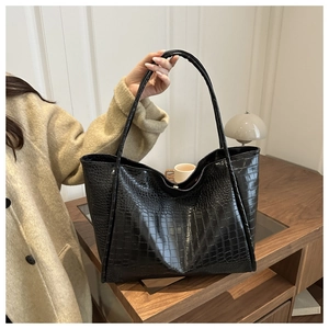 Detail of black crocodile embossed tote bag held by model in a chic office setting