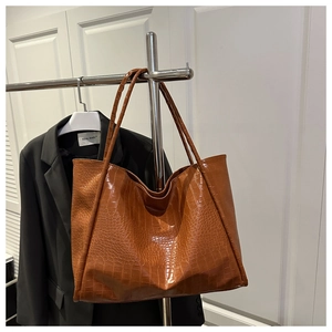 Macro detail of amber brown faux leather tote bag with embossed crocodile pattern texture