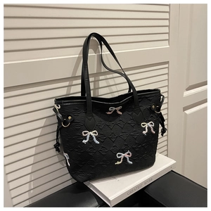 Detail of black quilted tote bag with colorful embroidered bows and drawstring sides