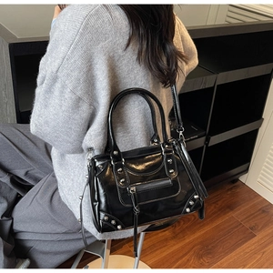 Vue détaillée des clous argentés et franges de zip sur un sac Boston noir brillant