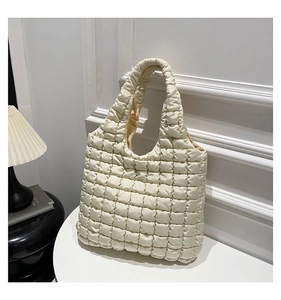 Detailed view of cream-colored quilted tote bag with pleated bubble texture on a white table