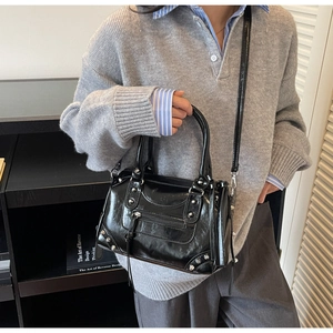 Détail du sac Boston noir brillant avec clous argentés porté par un mannequin