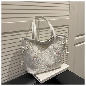 Detail of white quilted tote bag featuring embossed letters and colorful bow accents