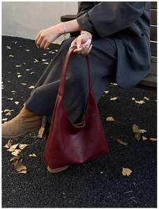 Detail of burgundy leather tote bag with embossed text on street background with ginkgo leaves