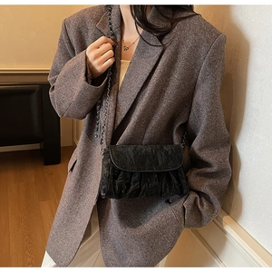 Detail of black pleated crossbody bag with silver chain strap worn by a model