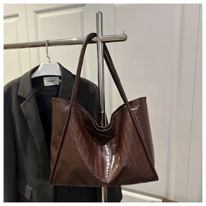 Close-up of large dark brown tote bag with crocodile texture hanging on a metal rack