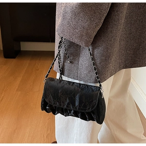 Detail of black pleated faux leather crossbody bag with silver woven chain strap