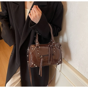 Sac Boston marron à rivets porté avec un blazer noir et des détails de pompons en cuir