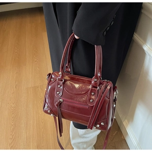 Détail du sac Boston rouge foncé en cuir brillant avec rivets et boucles argentées