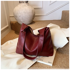 Detail of soft pleated dark red faux leather tote bag on white cloth and magazines