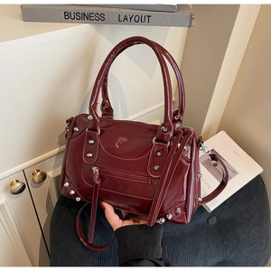 Gros plan du sac Boston en cuir verni bordeaux avec rivets métalliques et détails de glands