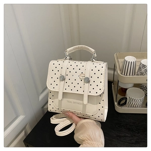 Close-up of a white polka dot mini bag with flap closure and adjustable long shoulder strap