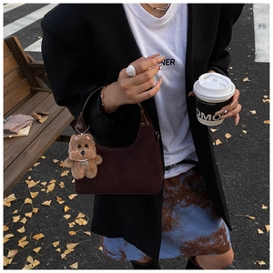 Close-up of brown suede hobo bag with teddy bear pendant and premium leather handle