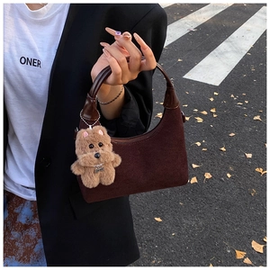 Detail of dark brown suede crescent bag with smooth leather handle and plush teddy charm