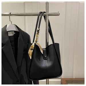 Detail of a black leather tote bag with a golden floral scarf on the stainless steel rack