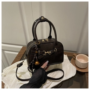 Détail d'un sac bowling vintage marron foncé avec mors doré et clochette sur tissu blanc
