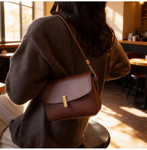 Lifestyle shot of a brown leather crossbody bag with a gold lock in a cozy cafe setting