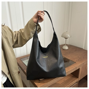 Detail of minimalist black PU leather tote bag with golden FASHION logo and wide strap